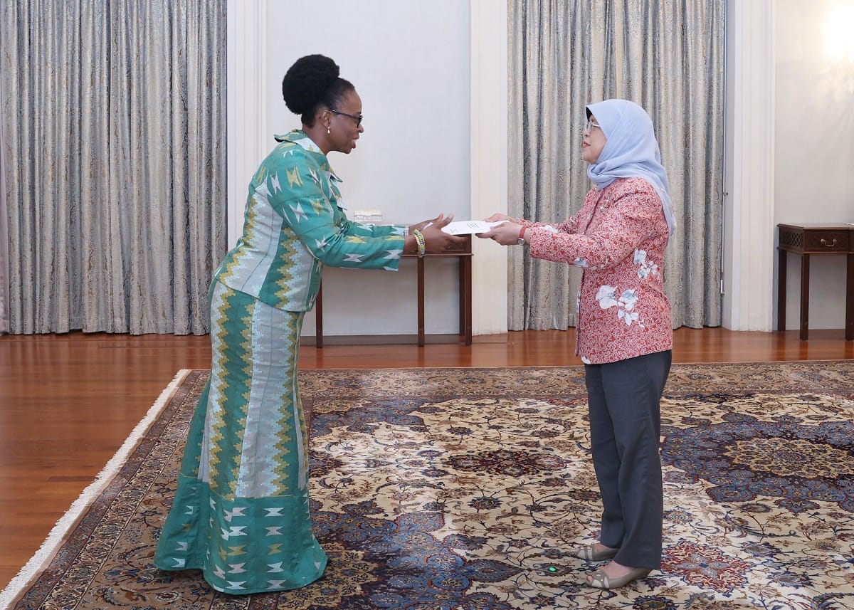 Two women exchanging a document in an ornate room.